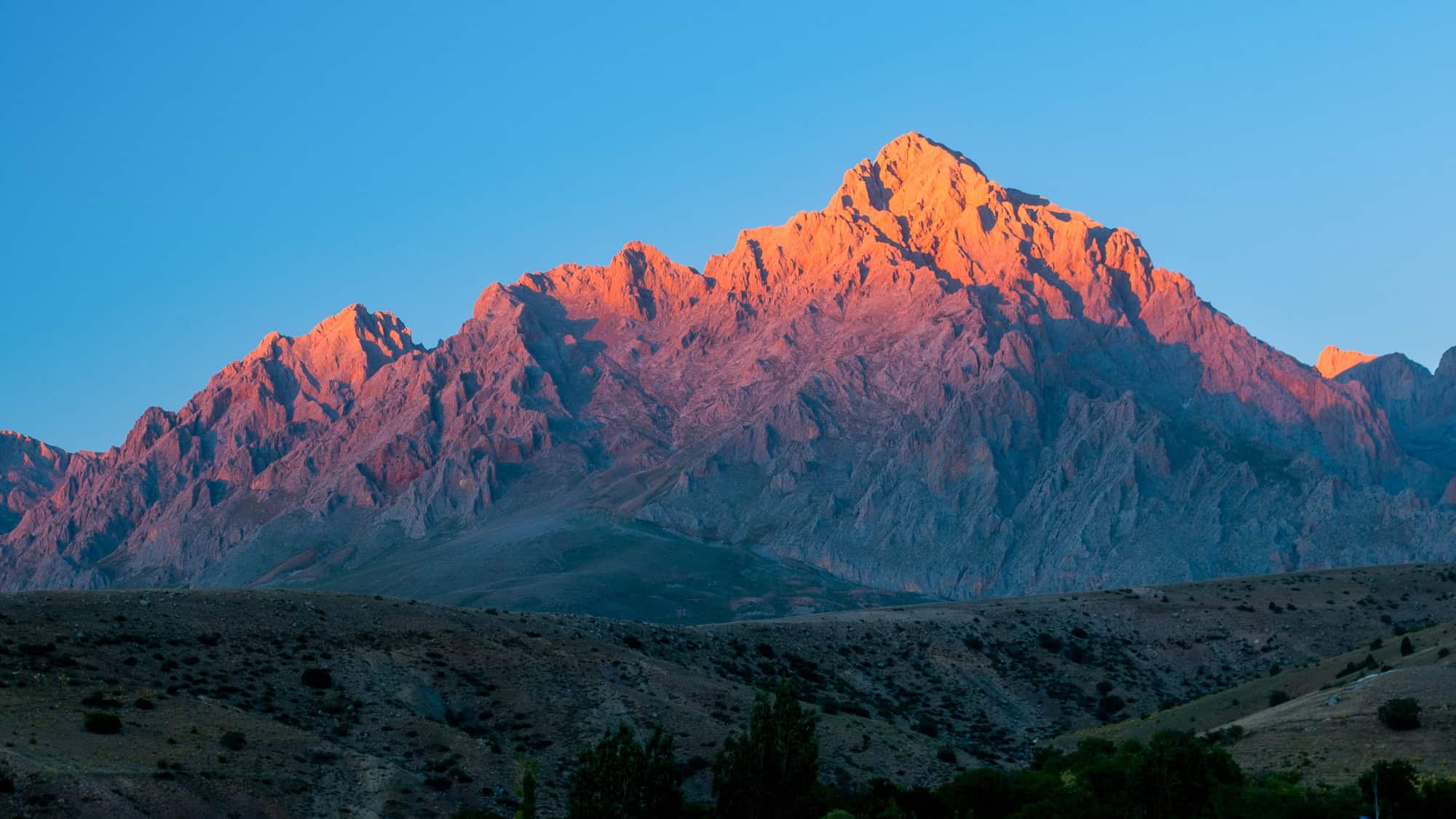 Jagged peaks glow with red-orange light from the setting sun against a clear evening sky.