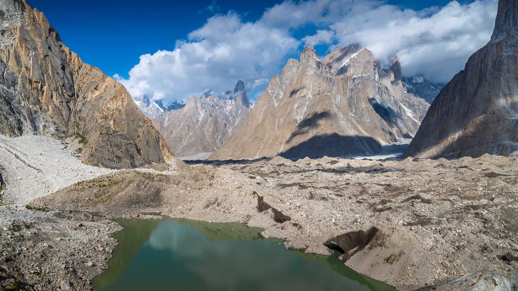 Sheer rock cliffs frame a glacier-fed lake with dramatic peaks rising through mist and clouds.