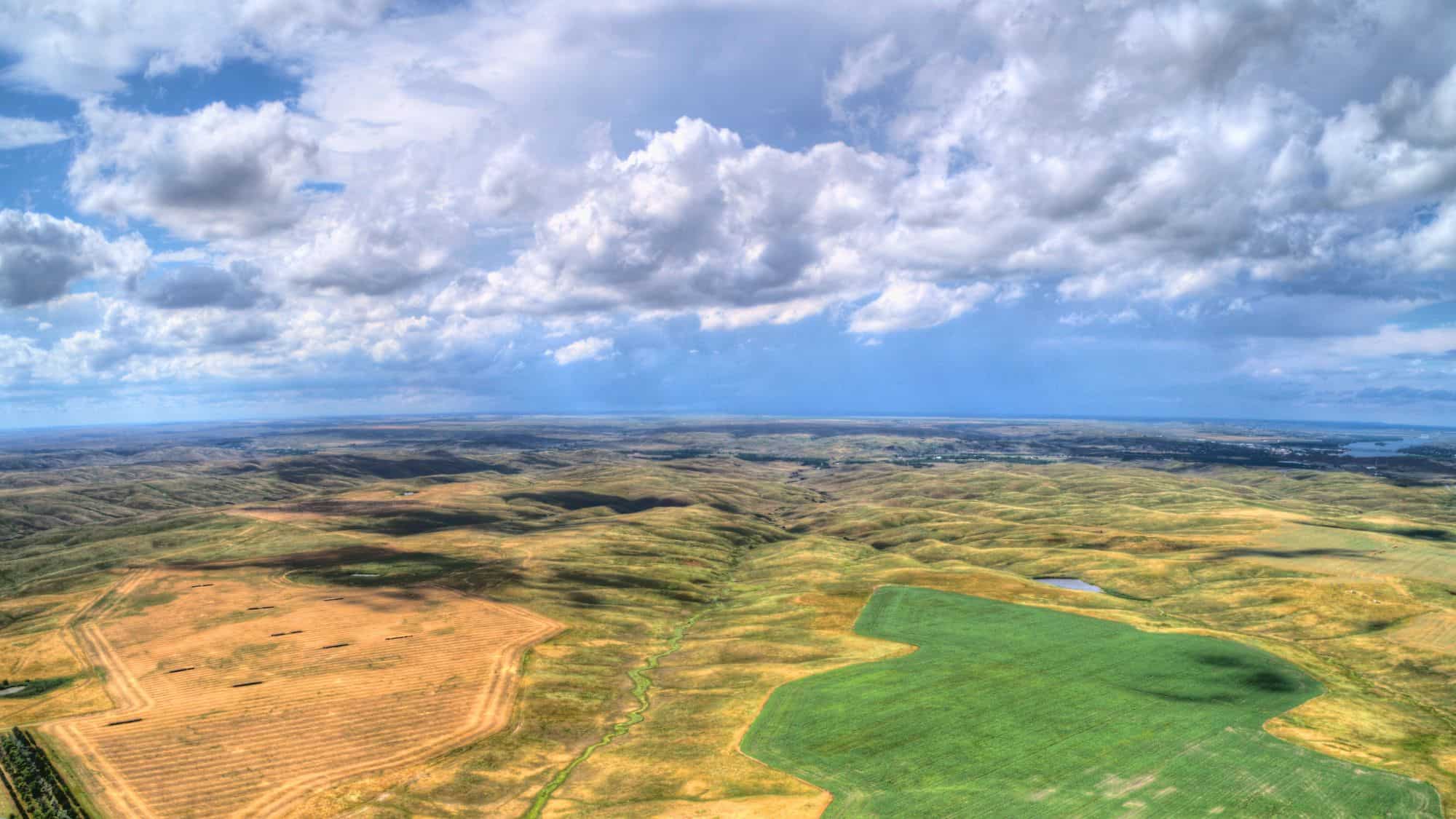Rolling plains stretch to the horizon with patches of farmland in shades of gold and green beneath dramatic clouds.