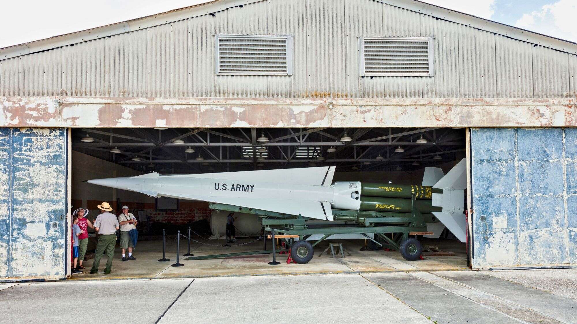 Visitors stand inside a hangar looking at a large U.S. Army missile displayed on a trailer.