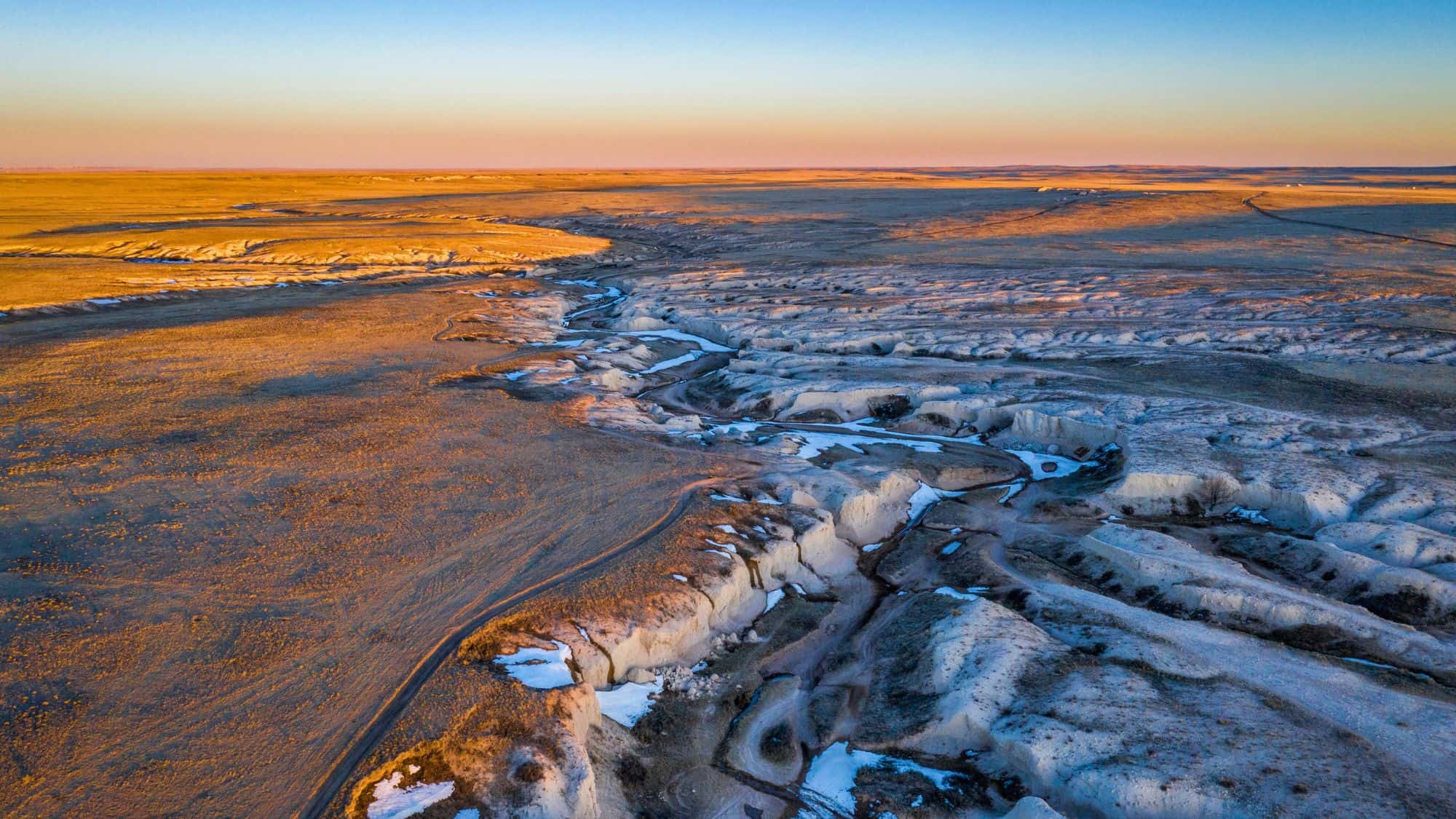Eroded white rock formations and gullies glow in the warm colors of a setting sun across open prairie.