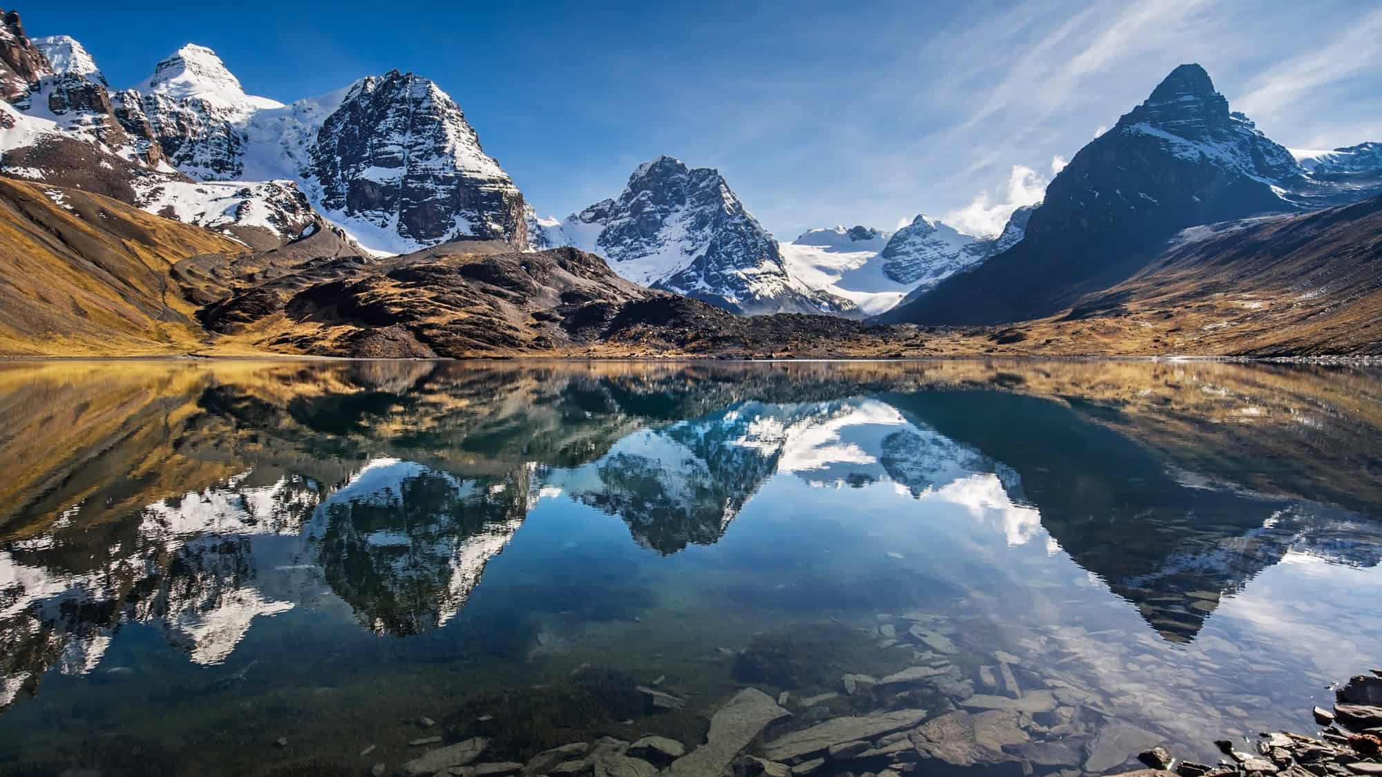 Snow-capped peaks are mirrored perfectly in a calm, crystal-clear alpine lake.