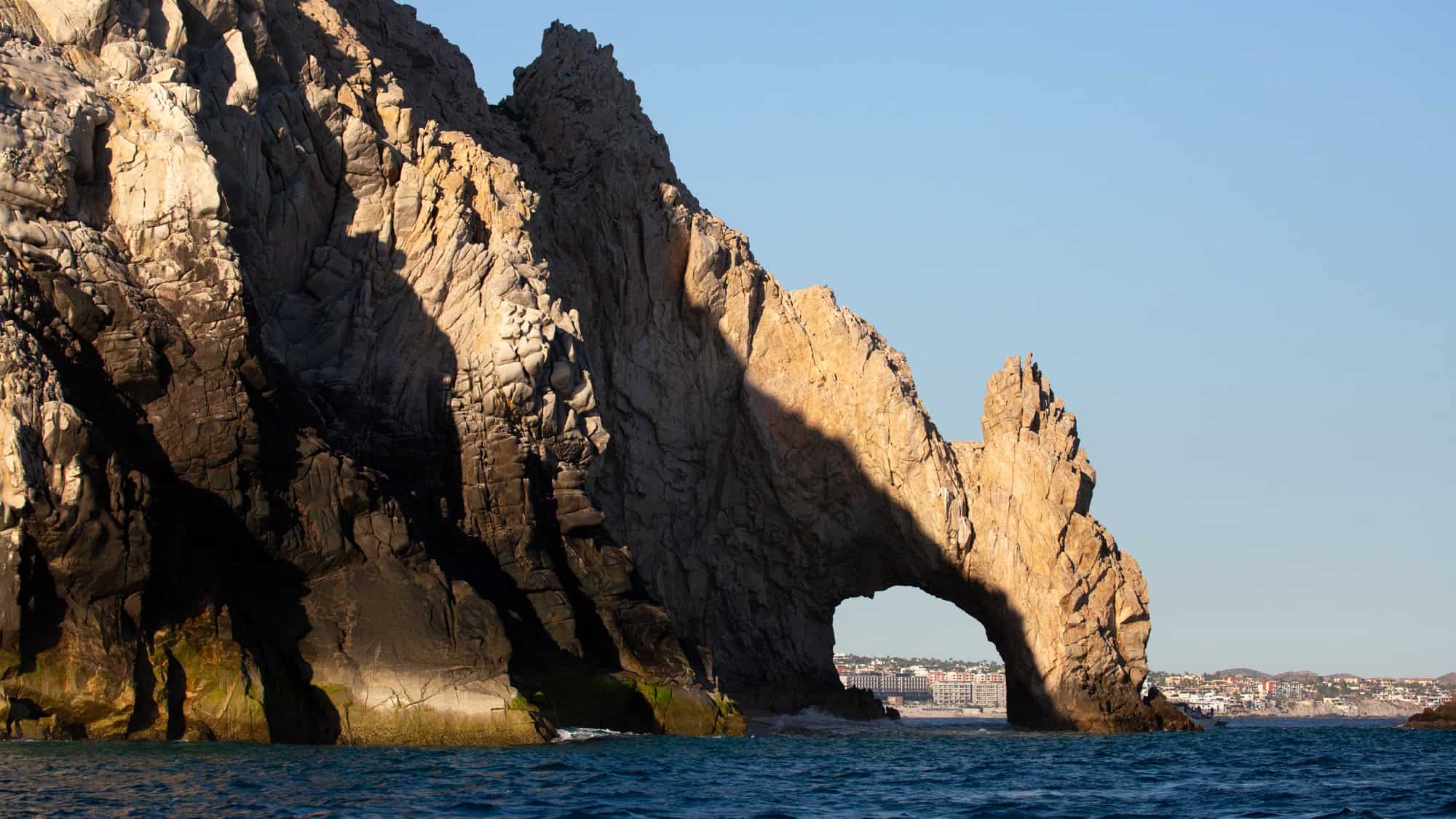The iconic El Arco rock formation juts into the sea, its natural stone arch glowing in the afternoon sun.