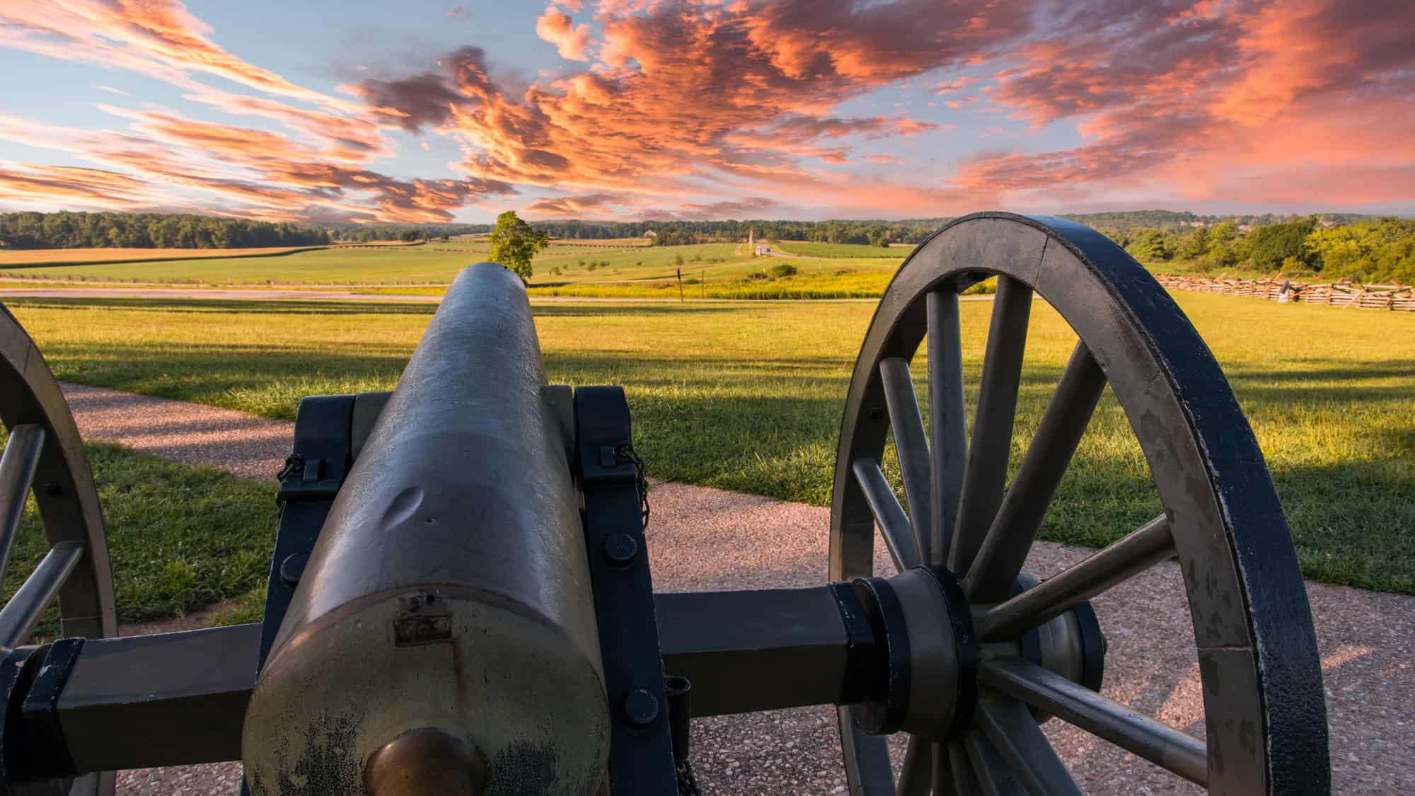 A view of an old cannon at Gettysburg battlefied at sunset under pink clouds.