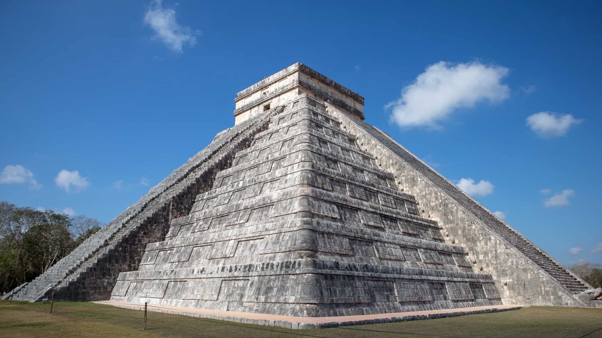 The Temple of Kukulcán stands tall under a bright blue sky, showcasing its steep stone steps and symmetrical design.
