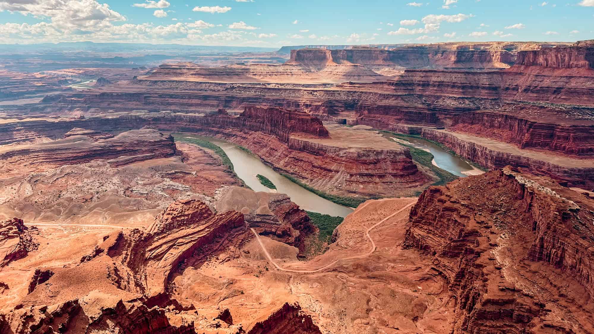 A sweeping view of the Colorado River winding through layered red rock canyons under a bright desert sky.