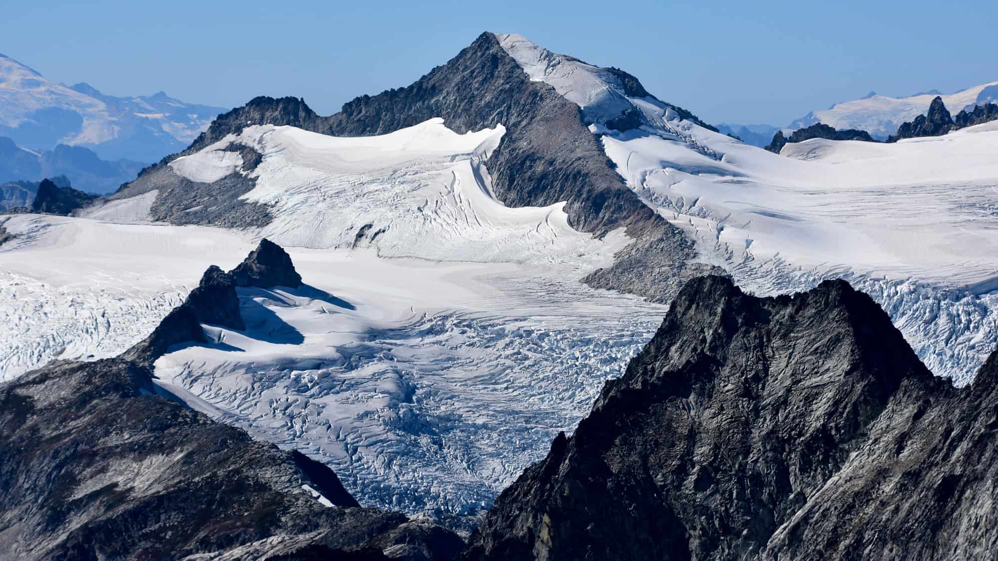Jagged mountain ridges are capped with massive glaciers, their icy crevasses spilling into valleys below.