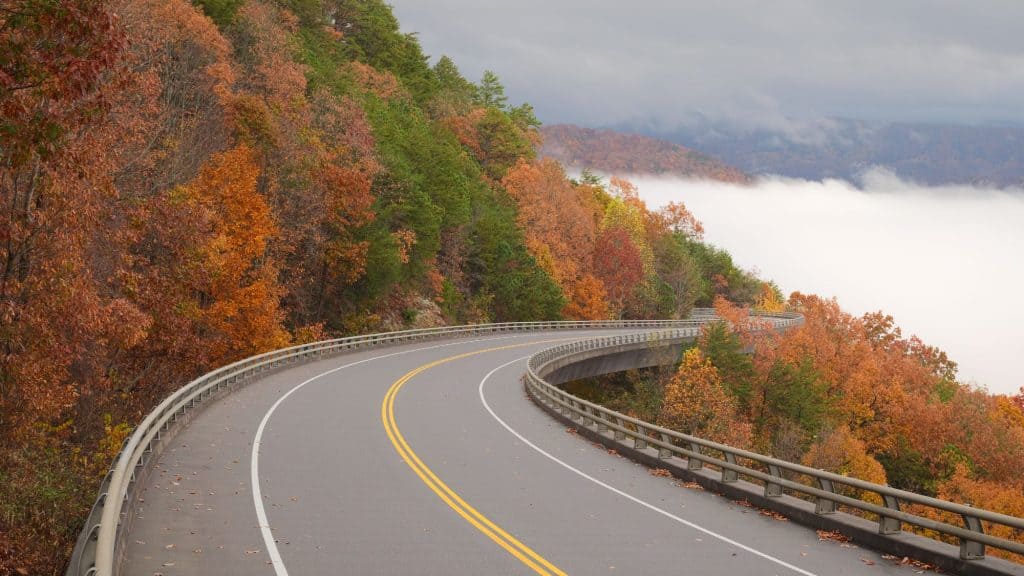 A road through Great Smoky Mountains National Park surrounded by colorful fall trees on one side and mist on the other.