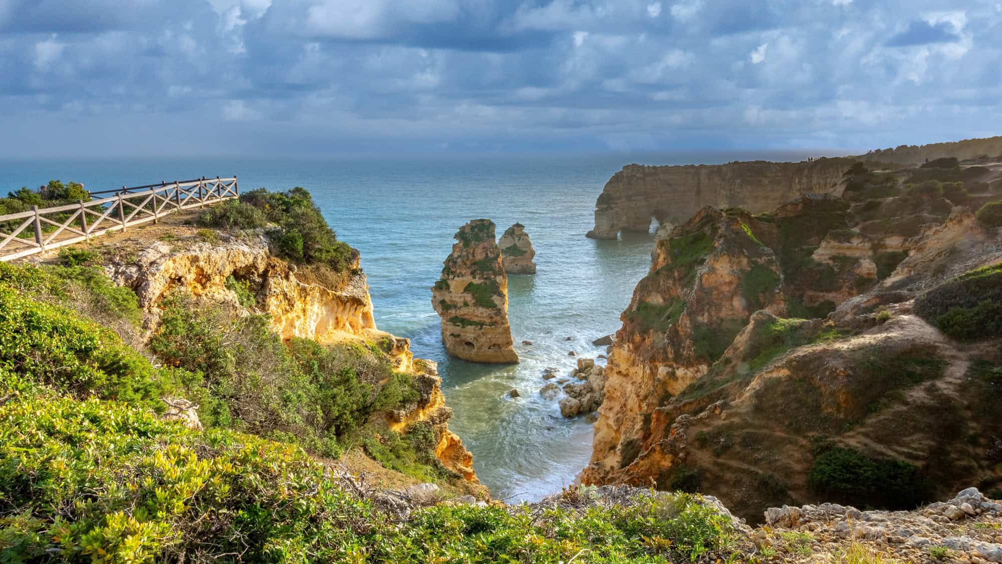 Golden sea stacks rise from emerald waters along a dramatic and rugged coastline in Portugal’s Algarve region.