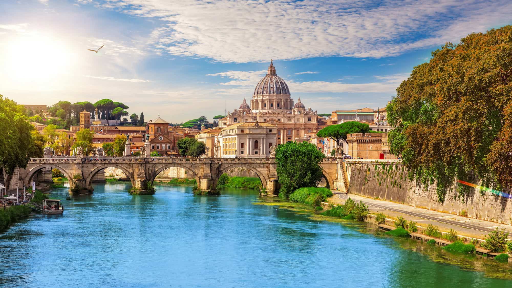 St. Peter’s Basilica dominates the skyline as the Tiber River flows under Ponte Sant’Angelo in Rome.