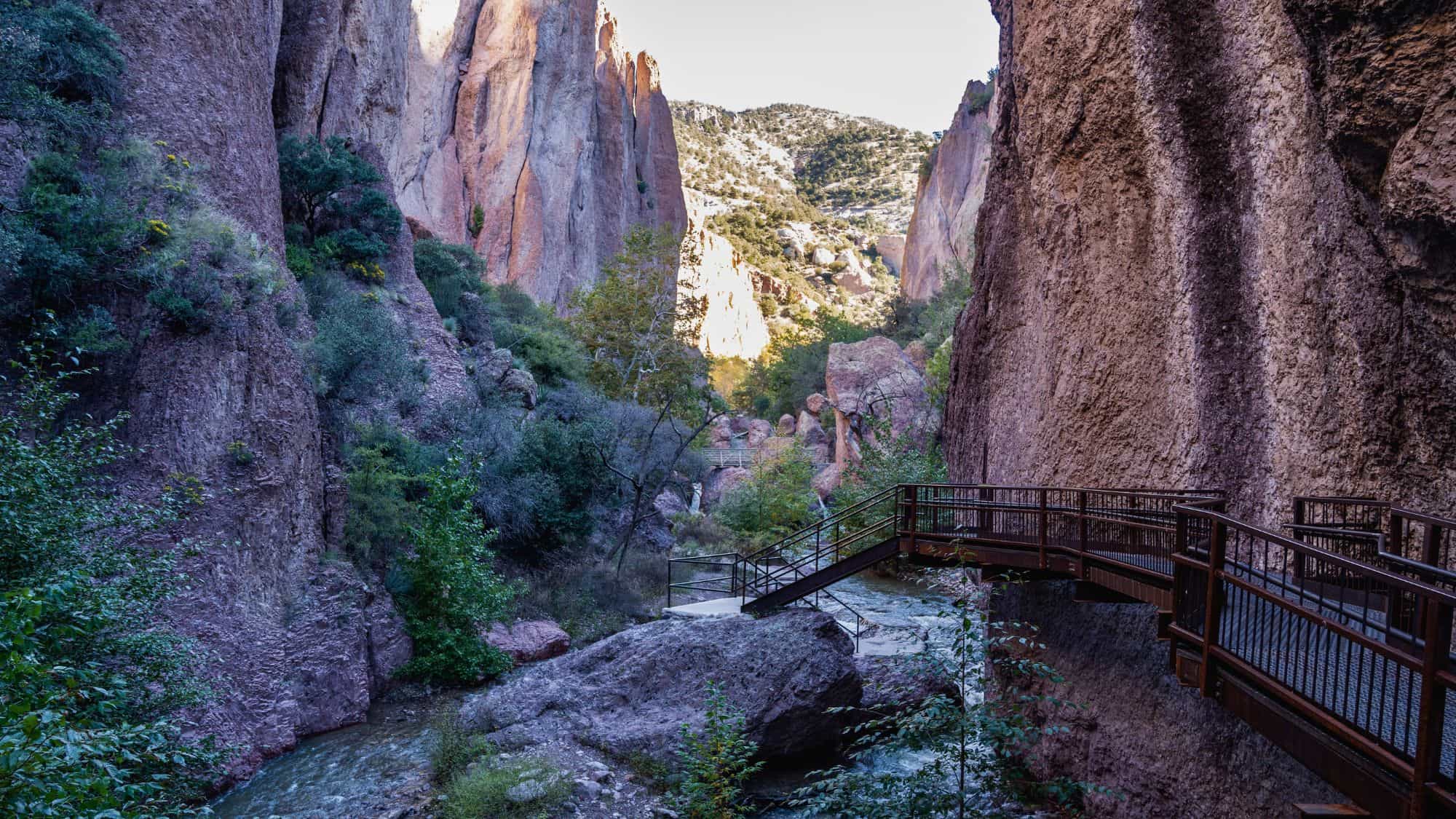 Golden evening light highlights a rocky bluff surrounded by vibrant fall foliage, with a rustic wooden pergola partially in view.