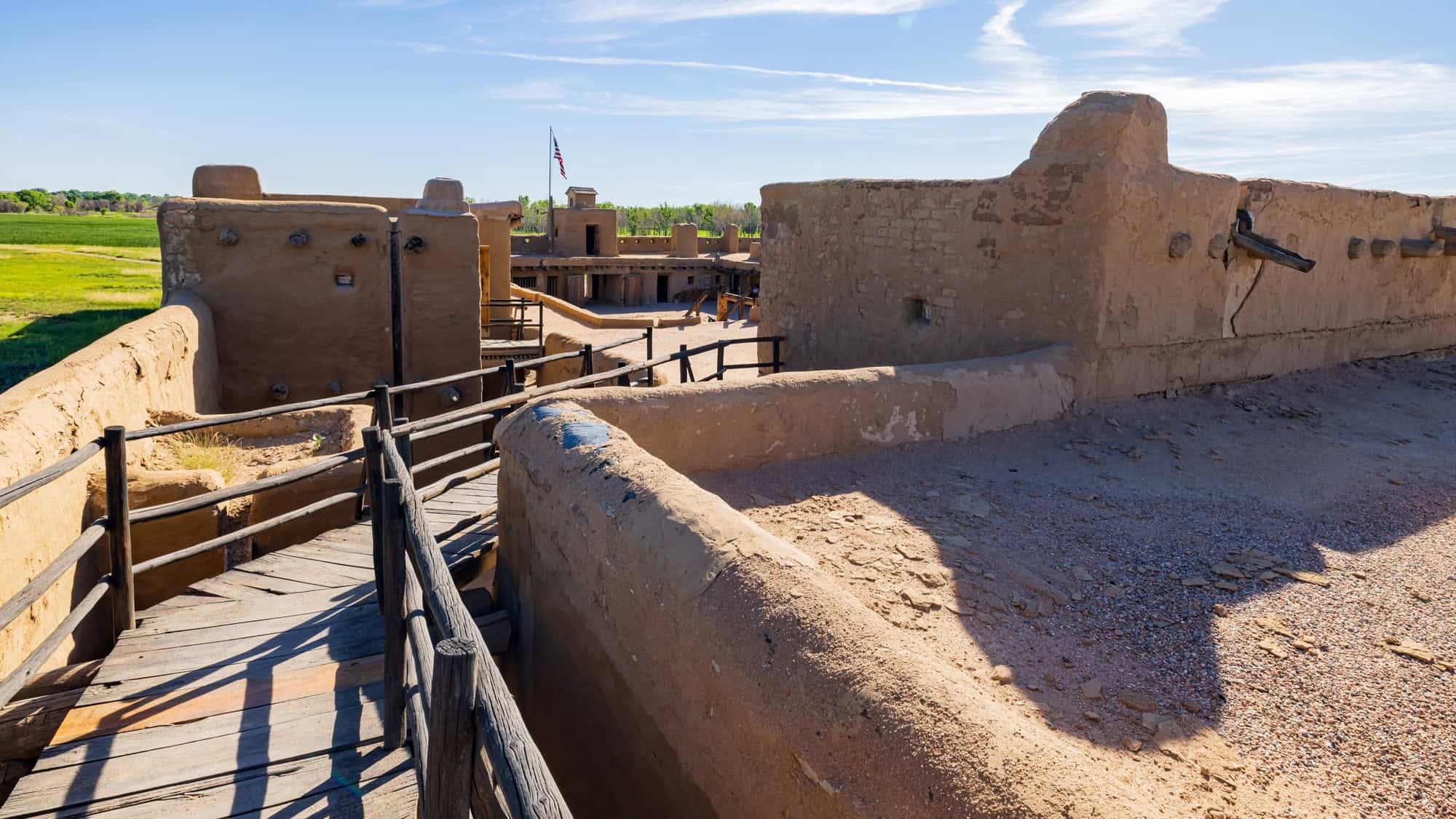 Adobe walls and wooden walkways frame the reconstructed Bent's Old Fort, a 19th-century trading post on the Santa Fe Trail surrounded by open plains.
