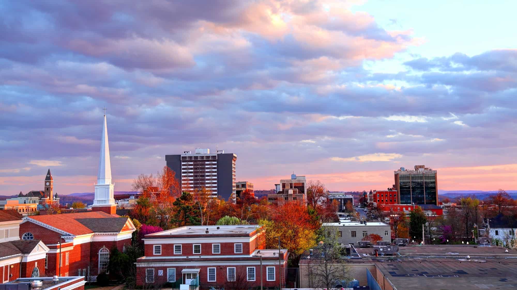 Mid-rise buildings, historic churches, and blooming trees create a colorful cityscape at sunset in downtown Fayetteville, Arkansas.