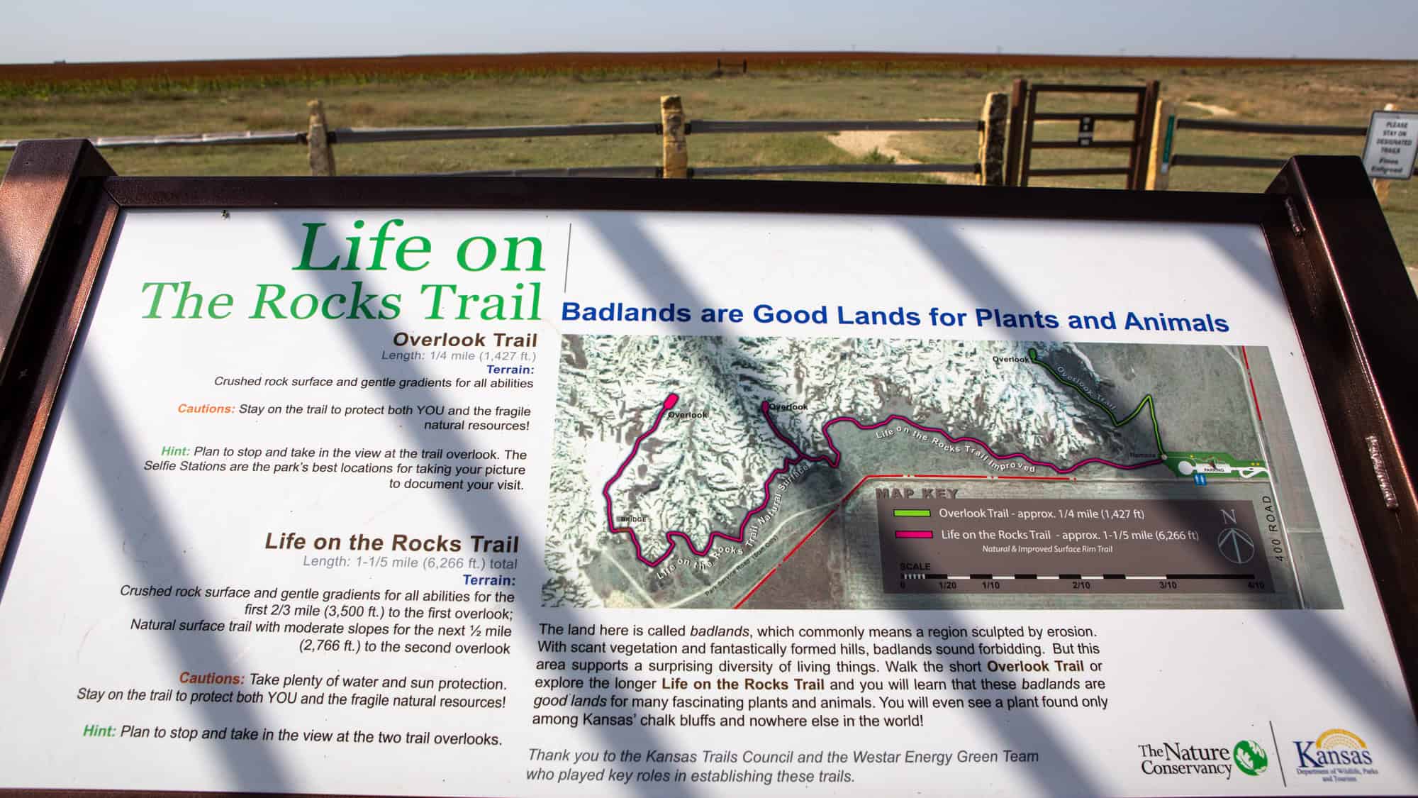 An informational trail sign titled "Life on the Rocks Trail" describes two hiking routes through Kansas badlands, with a color-coded map and guidance for trail users.