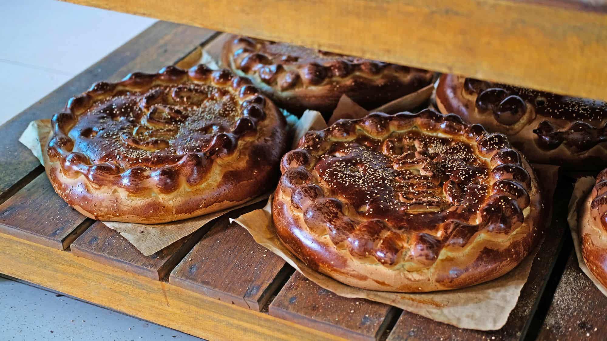 Golden brown round breads with decorative braided edges rest on parchment-lined wooden shelves, glistening with a glossy baked finish.