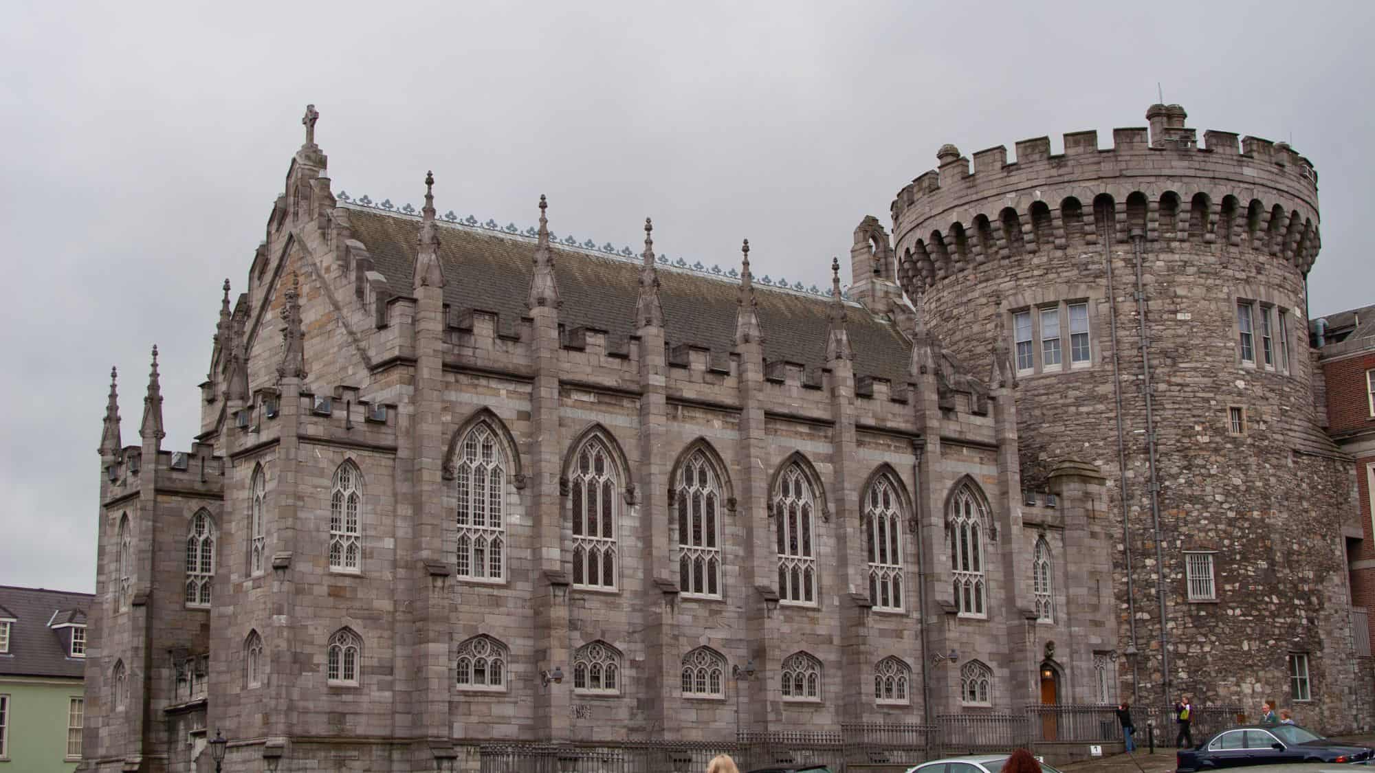 Historic stone architecture blends Gothic windows with a medieval round tower under a gray sky.