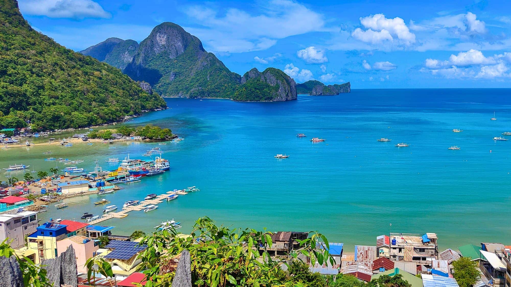 Vivid turquoise waters lap against the shores of El Nido, where traditional boats gather near steep, green-covered limestone islands.