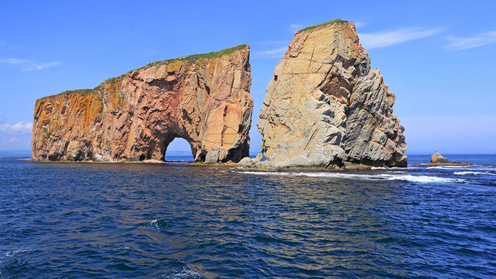 Towering limestone cliffs rise from the Gulf of St. Lawrence, with a dramatic sea arch and separated pillar forming one of Canada's most iconic coastal landmarks.