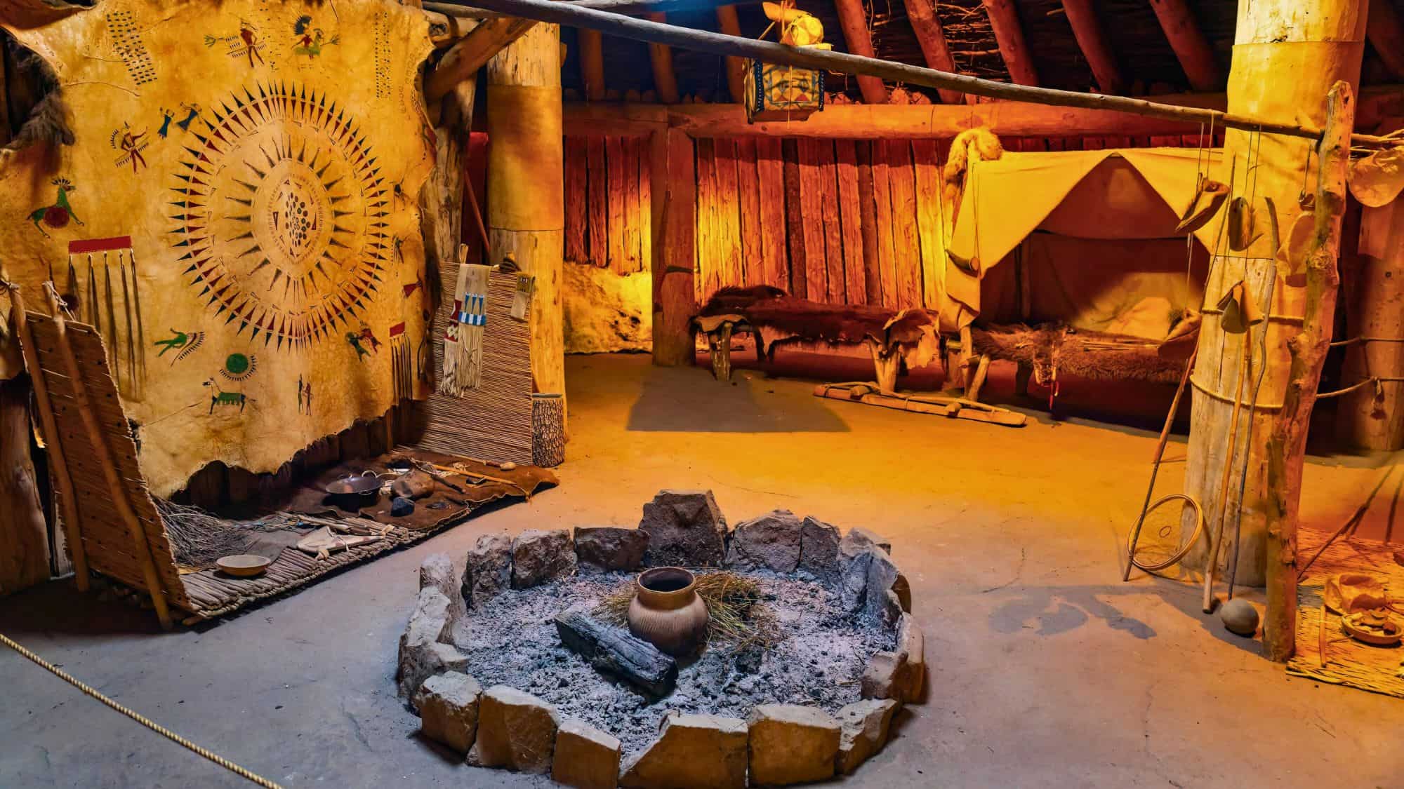 Inside a reconstructed earth lodge, animal hides, hand-crafted tools, and a central hearth showcase the traditional living space of Plains tribes.