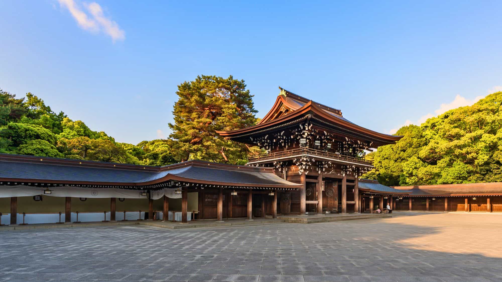 This wooden Shinto gate and courtyard are surrounded by tranquil greenery and a bright blue sky.