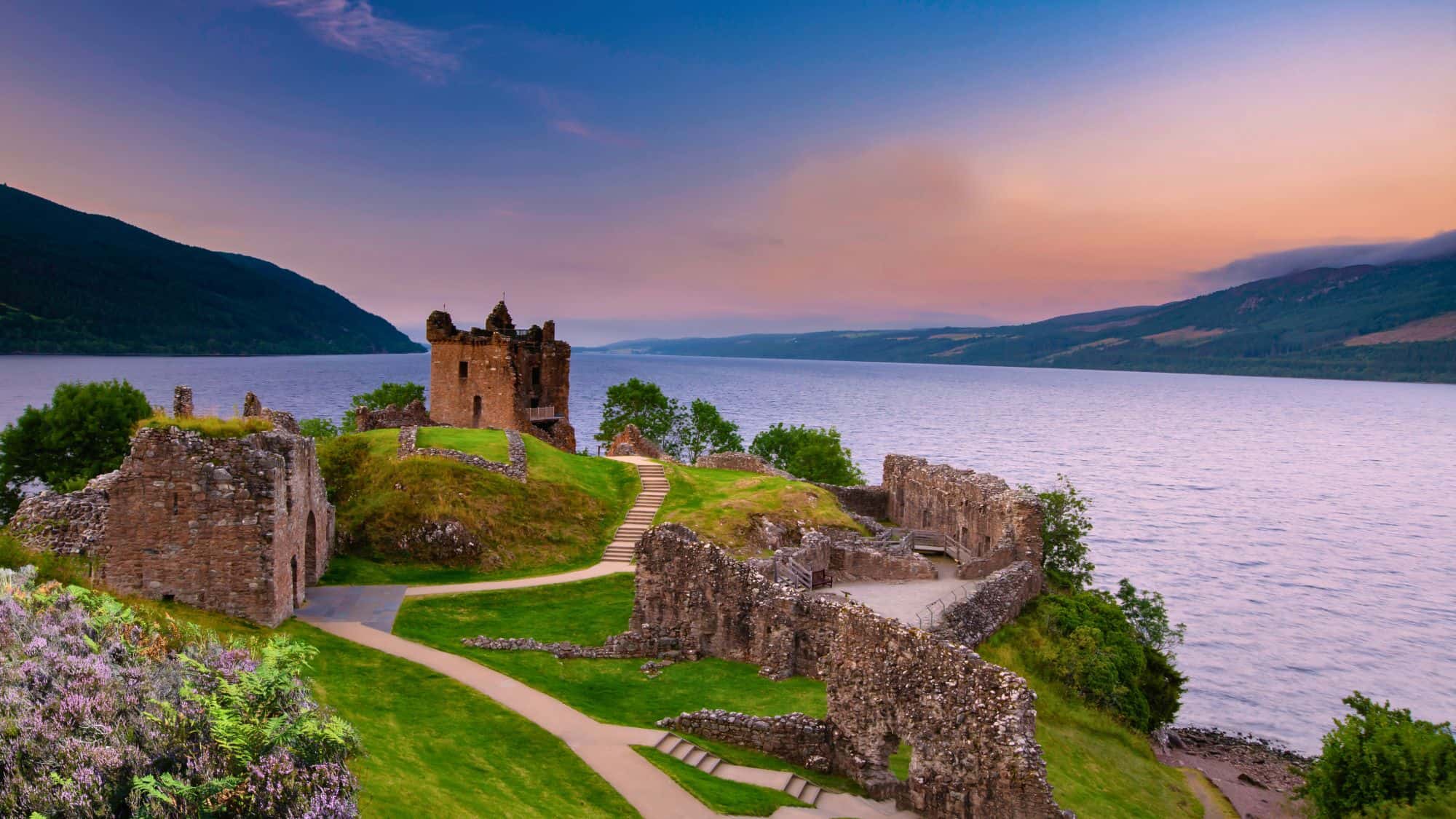 Set on the banks of Loch Ness, Scotland, the remnants of Urquhart Castle stand against the fading light, surrounded by calm waters and rolling hills.
