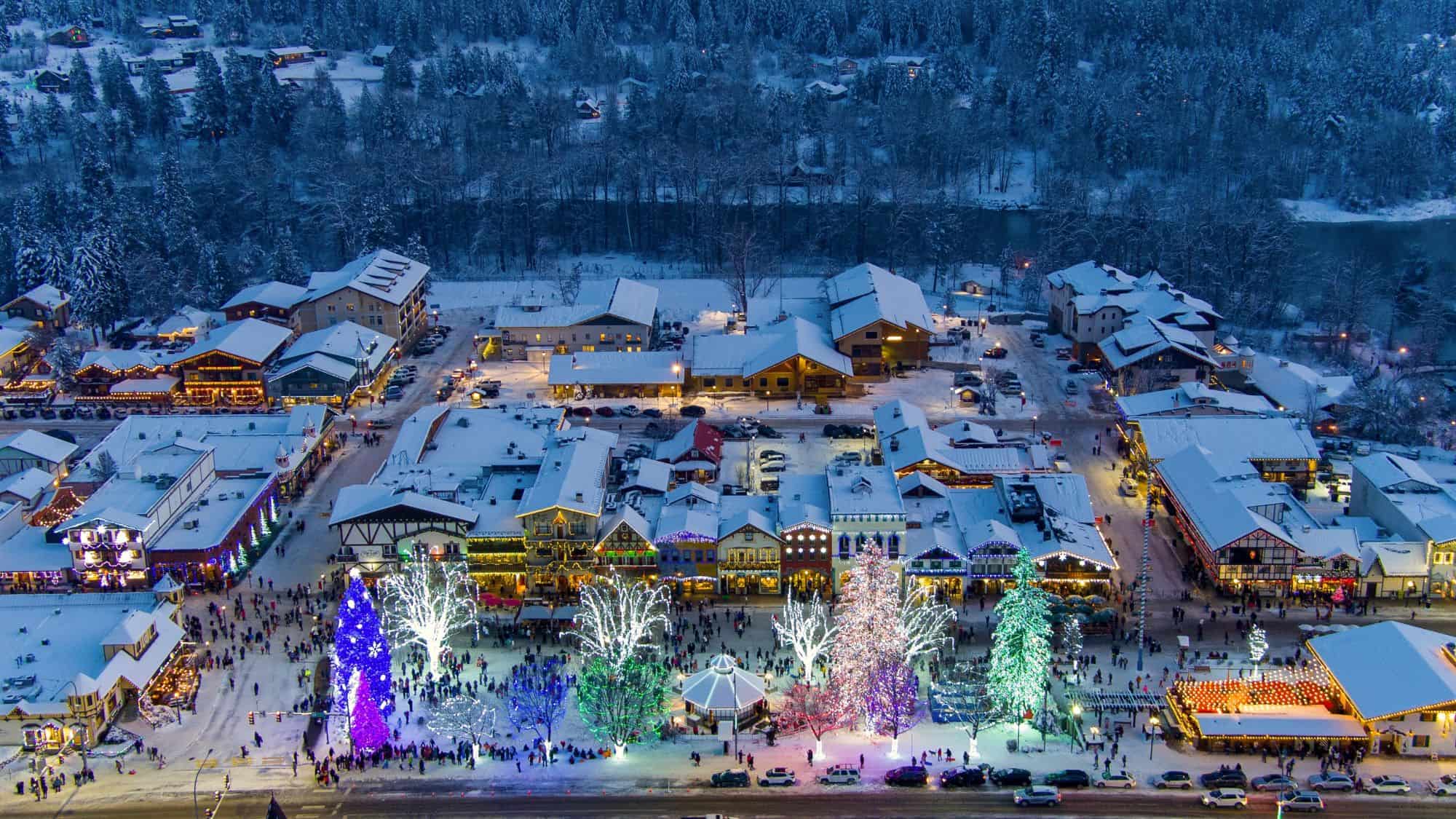 Strings of lights and colorful decorations line the snowy Bavarian-style streets of Leavenworth, Washington, bustling with visitors during winter festivities.
