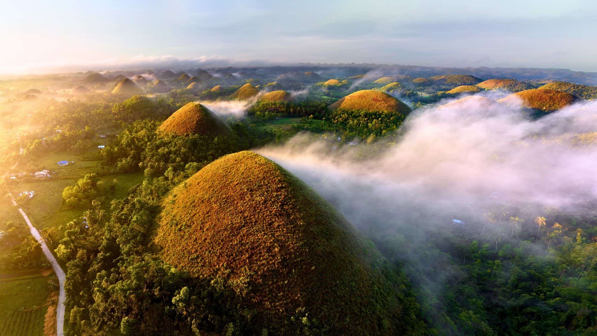 Rounded grassy hills spread across the landscape like mounds in a fantasy world, bathed in early sun and partially veiled by drifting mist.