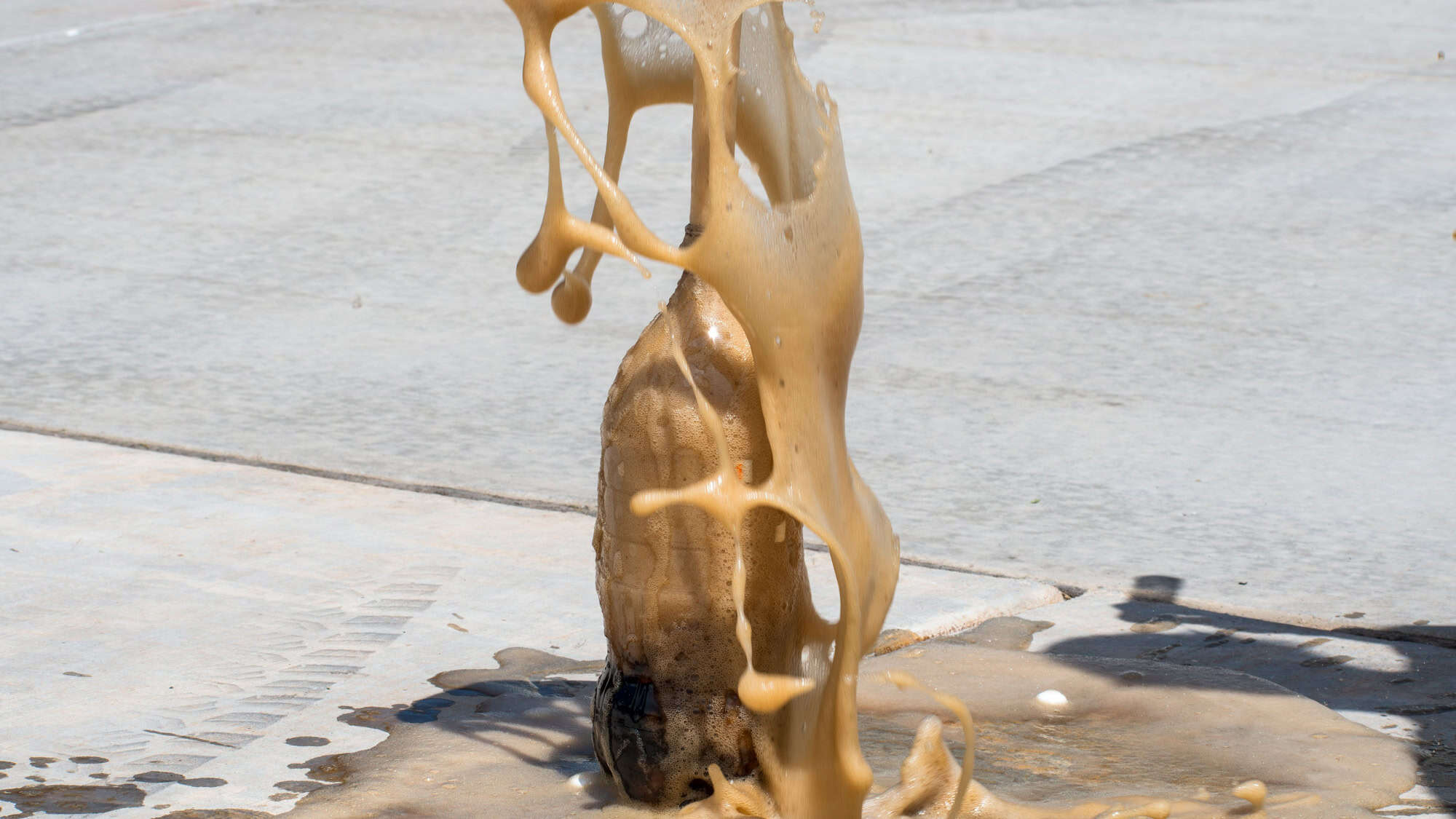 An explosion of pop happens when mentos interact with diet soda creating a geyser out on the sidewalk.